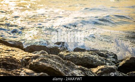 Farbfoto des Meer Spritzwasser über große Felsblöcke für Rock Buhnen auf branksome Chine Beach, Poole, England verwendet. Stockfoto