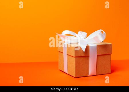 Trendige attraktive minimalistische Geschenk auf dem orangen Hintergrund. Frohe Weihnachten, Valentinstag, Geburtstag und andere Feiertage Konzept. Stockfoto