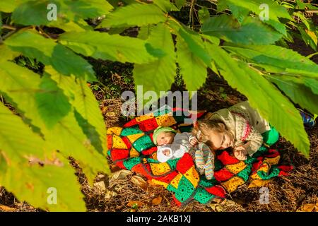 Branksome Chine Gardens, Poole, Dorset, England - 19. Oktober 2019. Ein Kind und Neugeborener liegen auf bunter Strickdecke unter Buchsenbäumte Sonne. Stockfoto