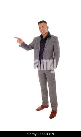 Ein hübscher junger Mann, der mit den Händen in seiner Tasche in einem grauen Anzug, zeigt mit einer Hand auf weißem Hintergrund Stockfoto