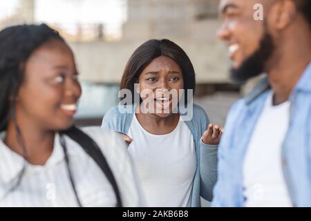 Eifersucht Konzept. Grumpy schwarze Mädchen wütend zu ihrem Freund, flirten mit einer anderen Frau, stehend mit wütenden Gesichtsausdruck auf Hintergrund Stockfoto