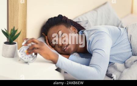 Schlecht Schlafen. Afro Frau Ausschalten Weckdienst berühren Kopf Aufwachen im Bett im Schlafzimmer. Selektiver Fokus Stockfoto