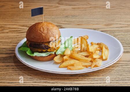 Doppelter Rinderburger mit Doppelkäse und Salat. Serviert mit Kartoffeldippern auf dem Holztisch in der weißen Platte. Amerikanische Küche. Stockfoto