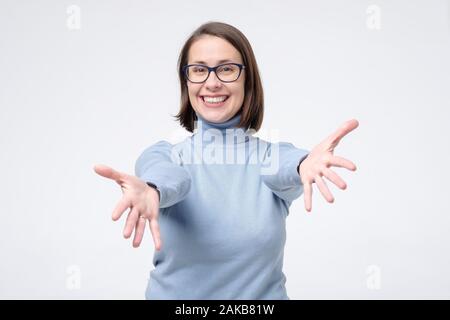 Freundlich , reife Frau in Gläser verteilen Hände seitlich zu umarmen, fröhlich lächelnd knuddeln, willkommen oder jemanden grüßen stehend weiß backgro Stockfoto
