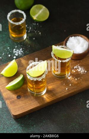 Mexikanische Gold Tequila shot mit Kalk und Salz auf dunklem Stein Hintergrund. Stockfoto