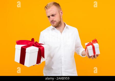 Junge schöne Mann hält zwei weißen Felder mit Geschenken und wählt auf gelbem Hintergrund Stockfoto