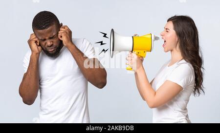 Wütende Frau schrie ihre afro Freund mit Lautsprecher, Nervenzusammenbruch oder PMS, zusammen über hellen Hintergrund stehend, Panorama Stockfoto