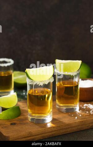 Mexikanische Gold Tequila shot mit Kalk und Salz auf dunklem Stein Hintergrund. Kopieren Sie Platz. Stockfoto