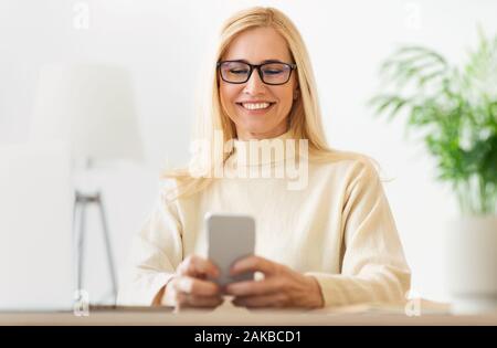Frau mittleren Alters surfen auf Handy, Brille und lächelnd Stockfoto