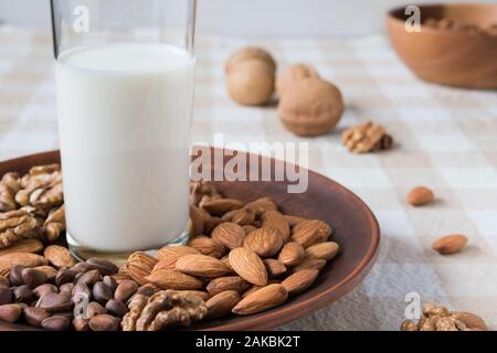 Gesunde Ernährung Konzept, Mandeln, Pinienkerne, Walnüsse und ein Glas Milch auf einem Teller auf den Tisch Stockfoto