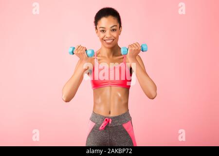 Training. Lächelnd Afro Girl tun Hantel Bizeps curl Übung über Rosa Hintergrund. Studio Shot Stockfoto