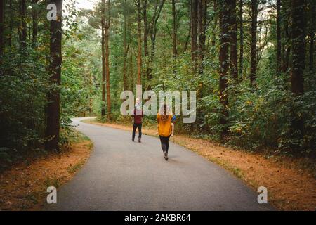 Rückansicht einer Familie, die im Herbst durch einen verwinkelten Waldweg geht Stockfoto