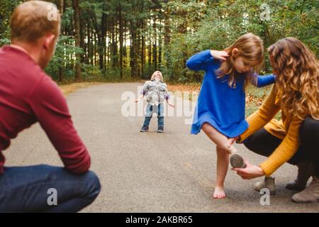 Eine Mutter hilft ihrem Kind mit einem Schuh, während ein Kleinkind einen Wutanfall wirft Stockfoto