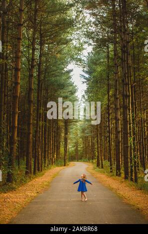 Ein kleines Mädchen wirbelt in einem blauen Kleid in einem magischen Pinienwald Stockfoto