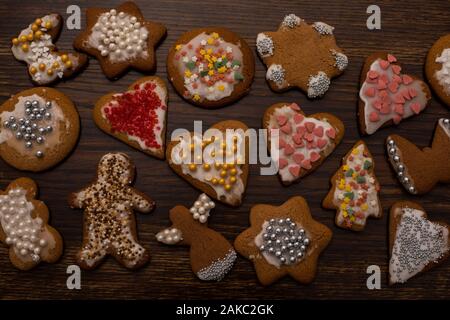 Hausgemachtes Lebkuchen in verschiedenen Formen mit weißer Vereisung und buntem Zuckerdekor auf dem Hintergrund eines alten Holztisches Stockfoto