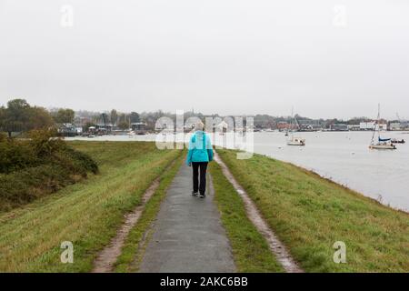 Eine einsame Frau mittleren Alters zu Fuß entlang eines Flusses Pfad an trüben und regnerischen Tag in Suffolk. Stockfoto