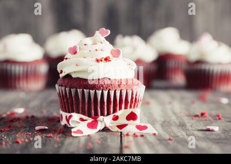 Red velvet Cupcakes mit Käse Zuckerguss dekoriert, herzförmigen Bonbons und Krümel auf einem rustikalen Holztisch. Valentines Dessert Stockfoto