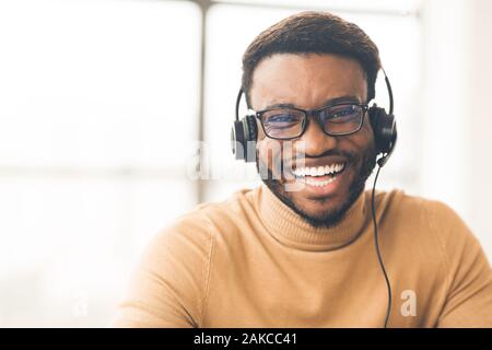 Helpline Konzept. Kopf geschossen von lächelnden Mann in Schwarz das Headset im Büro an der Kamera schaut. Der leere Raum Stockfoto