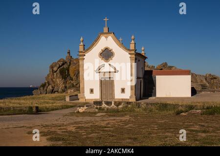 Kleine weiße Kapelle im traditionellen portugiesischen Stil an der Küste des Atlantik, neben einem Felsen. Strahlend blauen Himmel. Porto, Portugal. Stockfoto