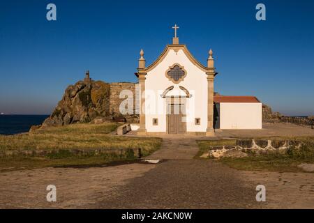 Kleine weiße Kapelle im traditionellen portugiesischen Stil an der Küste des Atlantik, neben einem Felsen. Strahlend blauen Himmel. Porto, Portugal. Stockfoto