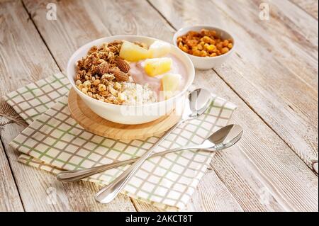 Gebackenes Müsli mit Nüssen, Hüttenkäse, Erdbeer Joghurt und Ananasscheiben in einer Platte auf einem karierten Serviette. Das Licht der Morgensonne. Gesundheit Stockfoto
