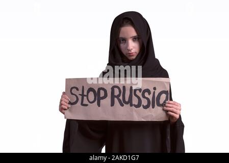 Muslimisch-arabischen Mädchen. Russland Aggressor. Arabische Trauriges Mädchen in schwarzen Abaya und weißen Hintergrund mit Plakat mit Plakat stoppen Russland, keinen Krieg. Stockfoto