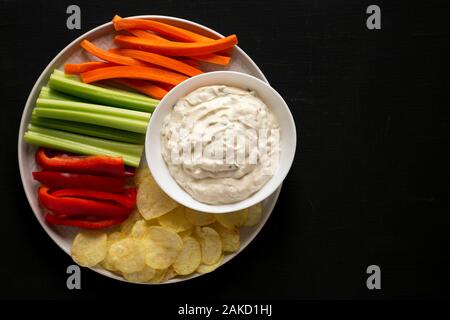 Hausgemachte karamellisierten Zwiebeln Dip mit Kartoffelchips, Sellerie, Paprika und Karotte auf schwarzem Hintergrund, Ansicht von oben. Flach, Overhead, von oben. Kopieren spac Stockfoto