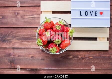 Erdbeeren und Liebe Sie Beschriftung. Weidenkorb mit reifen Erdbeeren auf Holz- Hintergrund. Obst und Liebe. Stockfoto