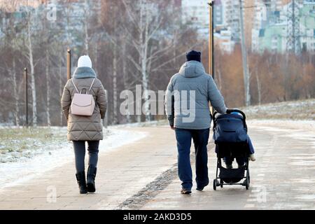 Paar mit einem Baby Stroller Walking im Winter Park während der. Schneewetter, Konzept der Mutterschaft, Eltern mit Kinderwagen Stockfoto