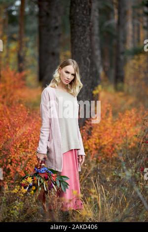 Mädchen gehen in den Wald. Einen schönen großen Blumenstrauß in den Händen einer Frau. Mädchen steht in Gelb, Rot, Gras, Herbst Natur Stockfoto