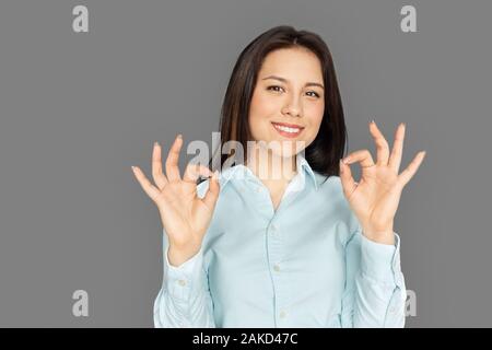 Freestyle. Junge Frau, die isoliert auf grau angezeigt ok Lächeln positive Stockfoto