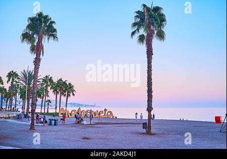 MALAGA, SPANIEN - 26. SEPTEMBER 2019: die lila Sonnenuntergang am Strand Malagueta mit Blick auf das ruhige Wasser des Meeres genießen, hohen Palmen und Malagueta si Stockfoto