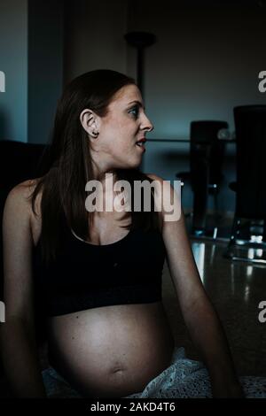 Junge nachdenklich schwangere Frau in Sportkleidung und sitzen auf dem Boden im Zimmer Stockfoto