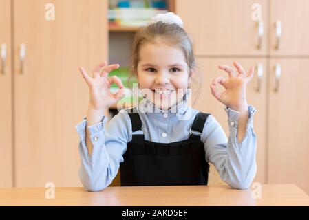 Mädchen Schülerin sitzt an ihrem Schreibtisch und zeigt die Zeichen in Ordnung. Stockfoto