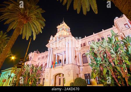 Die malerischen Gebäude von Malaga Rathaus mit Glockenturm, Spalten und Stuck Dekor in hellen Abend Leuchten, Spanien Stockfoto