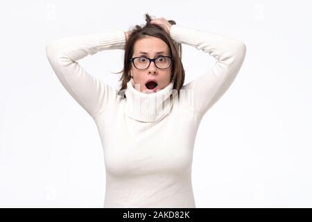 Junge kaukasier Frau in Gläser mit entsetzten Gesichtsausdruck mit Neuigkeiten überrascht wird. Studio shot Stockfoto