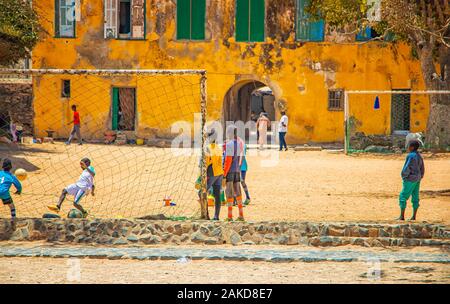 Insel Goree, Senegal - 22. April 2019: Unbekannter Jungs spielen Fußball auf dem Sand in der Stadt in Afrika. oys Spielen vor Ein altes gelbes Haus auf Stockfoto