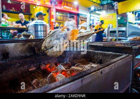 Bangkok/Thailand-December 2019: Fische drehen und Rösten über heiße Kohlen auf einem Grill in der Nähe einer Straße Restaurant in Chinatown in der Nacht. Stockfoto