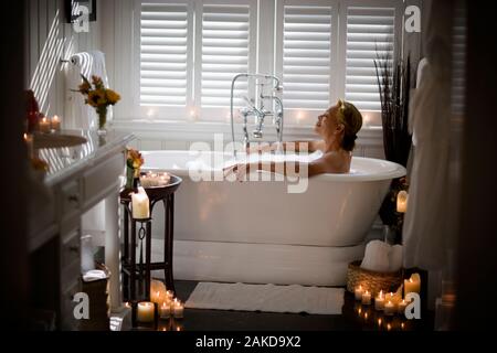 Erwachsene Frau, die sich in einem von Kerzen umgebenen Blasenbad entspannen kann. Stockfoto