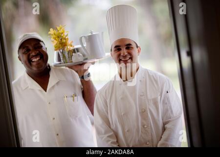 Porträt eines erwachsenen Mannes und einer jungen erwachsenen männlichen Chef holding Zimmerservice. Stockfoto