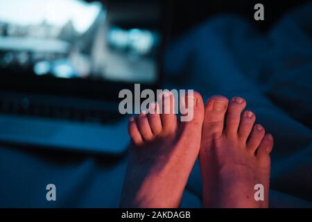 Nahaufnahme von Mann Zehen mit langen Ungeschnittenen Nägel, Pediküre dringend brauchen - zwei Meter neben einem Laptop in der Nacht sitzen mit neon leuchtend blau rot und Stockfoto