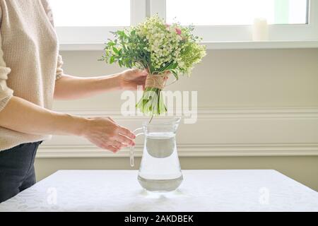 Frau Hände mit Blumenstrauß in der Vase auf dem Tisch Stockfoto