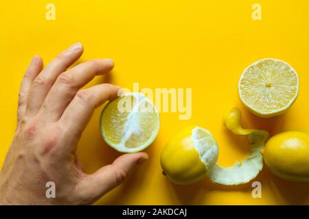 Blick von oben auf die männliche Hände, die ganze und aufgeschnittene reife Zitronen auf gelbem Untergrund, Konzept der Gesundheit und Vitamine Stockfoto