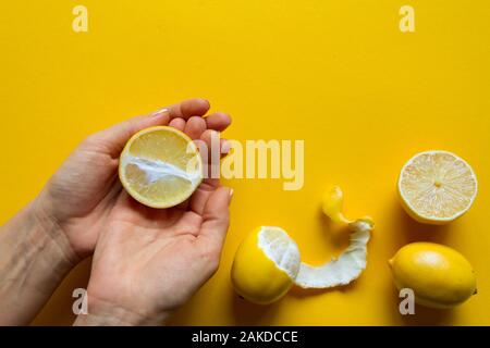 Blick von oben auf die weibliche Hände, die ganze und aufgeschnittene reife Zitronen auf gelbem Untergrund, Konzept der Gesundheit und Vitamine Stockfoto