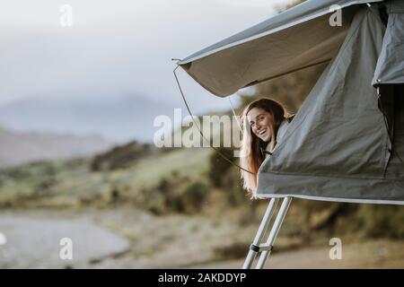 Eine junge lächelnde Frau steckt ihren Kopf aus einem Zelt in Neuseeland. Stockfoto