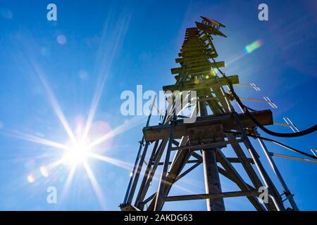 Ein niedriger Betrachtungswinkel und einer Funkübertragung Turm mit mehreren Antennen und einer Stahl Wartung Leiter, gegen einen strahlend blauen Himmel mit Sonne und lens flare Stockfoto