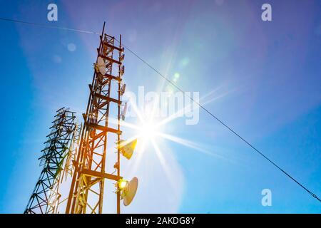 Eine niedrige Winkel aussicht auf zwei mobile Kommunikation Daten Sender und GPS-Signal Türme, gegen einen blauen Himmel mit hellen Sonne und bunten lens flare Stockfoto