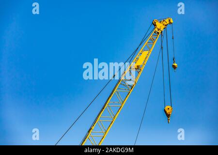 Eine Low Angle View auf der verlängerte Arm von einem gelben Turm Kran. Detail der oberen Riemenscheibe, Fock, Kerl, zurück bleiben, Hoist Seil und Haken. Im Bau. Stockfoto