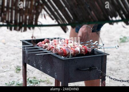 Grill im Freien auf hellen Sommertag. lecker saftig marinierte Stücke Fleisch, Tomaten, Zwiebeln, Paprika am Spieß braten auf Kohle. Camping, Holi Stockfoto