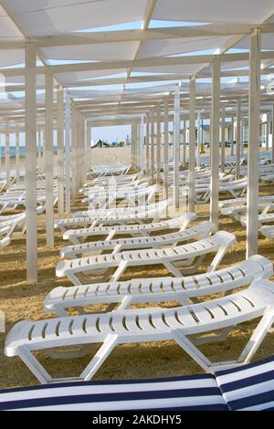 Weißen chaiselounges stehen in einer Reihe auf einem Sandstrand, Perspektive. Sommer, Urlaub am Meer Stockfoto
